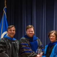 Provost Mili takes picture with 2 men on stage